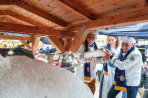 Das amtierende Stollenmädchen Nelly Köhler schneidet gemeinsam mit dem Vorstandsvorsitzenden des Schutzverbandes Dresdner Stollen, Andreas Wippler, und Ehrenmitglied Rudi Maas den Riesenstollen an.